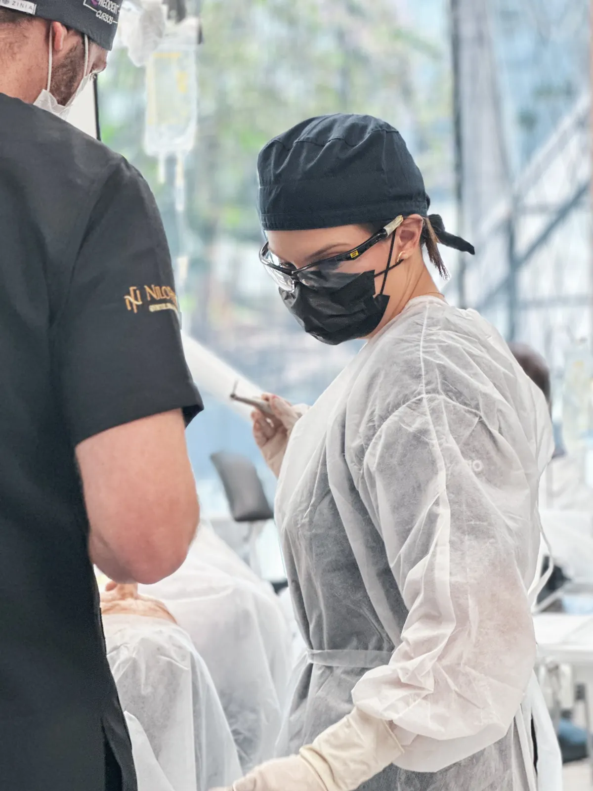 Profissional de avental descartável, touca e óculos de proteção acompanhando um procedimento