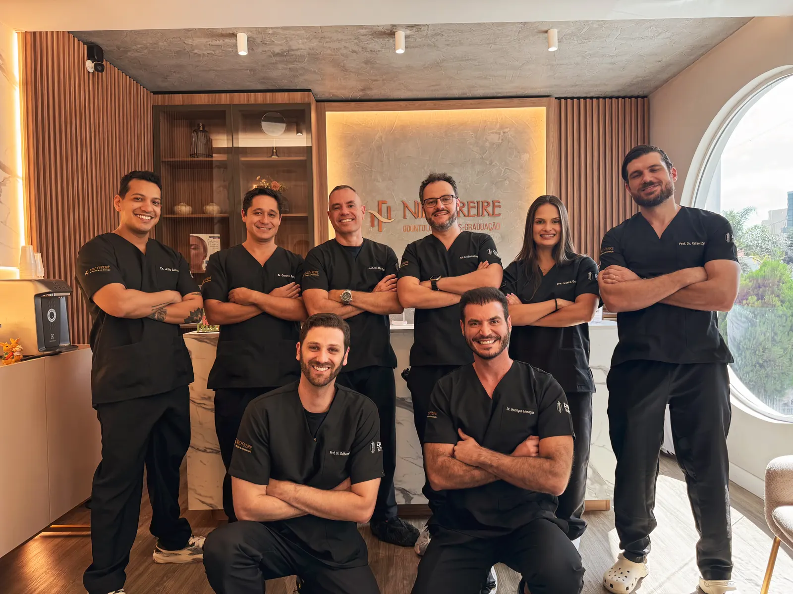 Grupo de oito profissionais de uniforme preto, em pé e agachados, diante do balcão da recepção